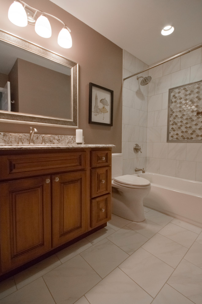 This is an example of a mid-sized transitional 3/4 bathroom in St Louis with raised-panel cabinets, medium wood cabinets, an alcove tub, a shower/bathtub combo, a one-piece toilet, beige tile, white tile, ceramic tile, brown walls, ceramic floors, an undermount sink, granite benchtops, beige floor and a shower curtain.