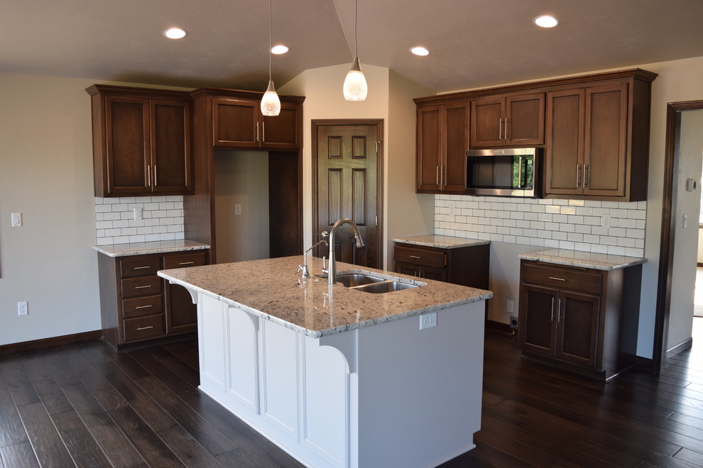 Open concept kitchen - large medium tone wood floor and brown floor open concept kitchen idea with an undermount sink, recessed-panel cabinets, medium tone wood cabinets, granite countertops, white backsplash, ceramic backsplash, stainless steel appliances and an island