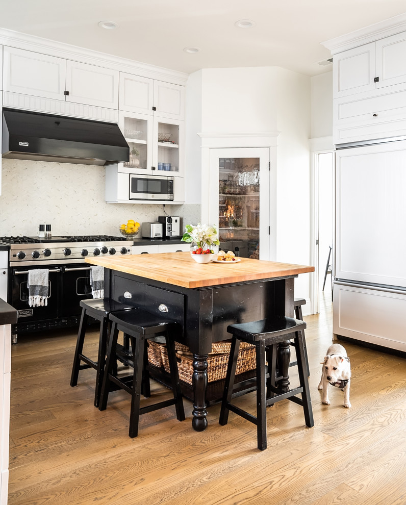 Inspiration for a mid-sized beach style l-shaped eat-in kitchen in Los Angeles with an undermount sink, shaker cabinets, white cabinets, white splashback, mosaic tile splashback, black appliances, light hardwood floors, with island, brown floor and black benchtop.