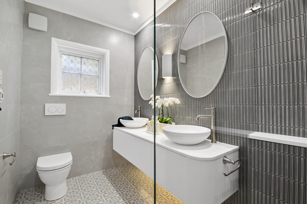 Пример оригинального дизайна: ванная комната среднего размера с фасадами с декоративным кантом, белыми фасадами, душем в нише, унитазом-моноблоком, разноцветной плиткой, керамической плиткой, разноцветными стенами, полом из керамической плитки, душевой кабиной, настольной раковиной, столешницей из искусственного камня, серым полом, открытым душем, белой столешницей, тумбой под две раковины, подвесной тумбой и потолком из вагонки
