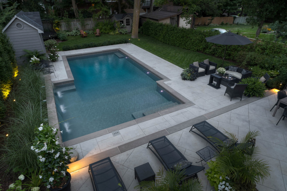 Inspiration for a mid-sized transitional backyard rectangular pool in Toronto with a water feature and stamped concrete.