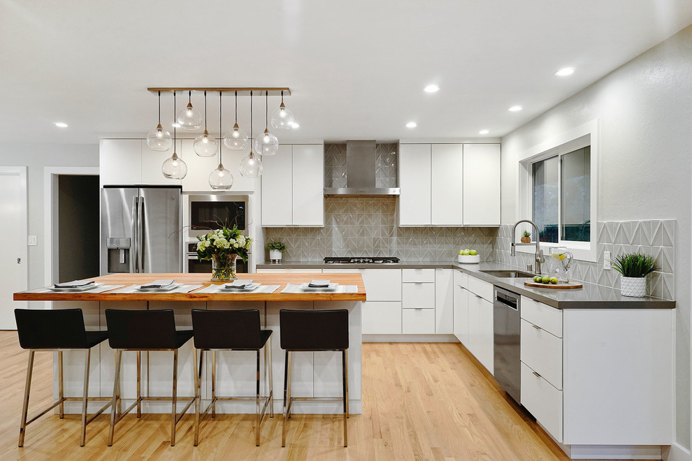 Design ideas for a contemporary l-shaped kitchen in San Francisco with a single-bowl sink, flat-panel cabinets, white cabinets, quartz benchtops, grey splashback, porcelain splashback, stainless steel appliances, light hardwood floors, with island, grey benchtop and beige floor.