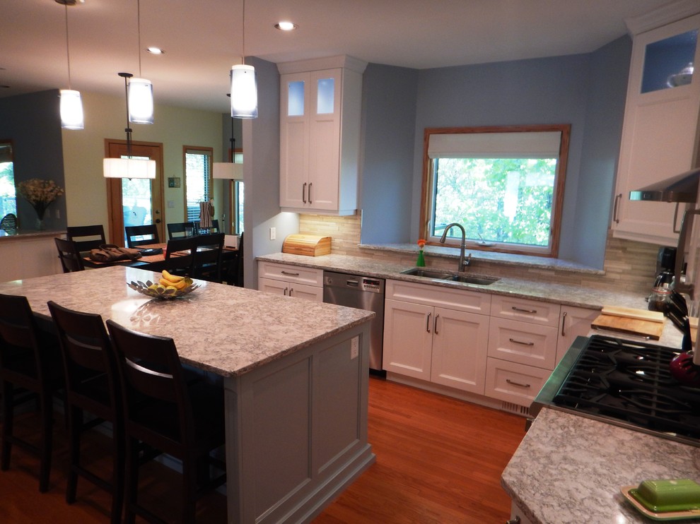 Inspiration for a large transitional l-shaped light wood floor eat-in kitchen remodel with an undermount sink, recessed-panel cabinets, white cabinets, quartz countertops, gray backsplash, stone tile backsplash, stainless steel appliances and an island