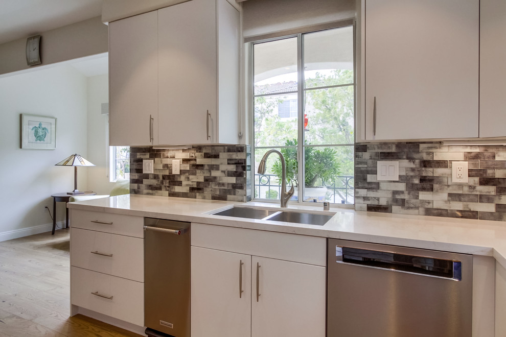 Mid-sized modern u-shaped eat-in kitchen in San Diego with an undermount sink, flat-panel cabinets, white cabinets, quartz benchtops, black splashback, glass tile splashback, stainless steel appliances, light hardwood floors, no island, brown floor and white benchtop.