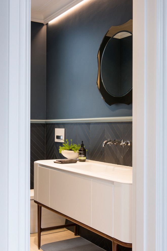 Design ideas for a small modern powder room in Sydney with furniture-like cabinets, white cabinets, a wall-mount toilet, blue tile, ceramic tile, blue walls, ceramic floors, an integrated sink, solid surface benchtops and grey floor.