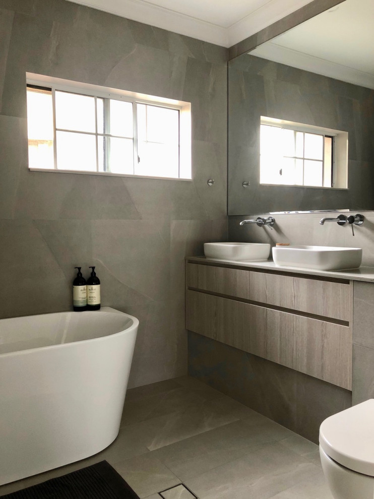 Photo of a medium sized contemporary shower room bathroom in Sydney with flat-panel cabinets, grey cabinets, a freestanding bath, a one-piece toilet, grey tiles, grey walls, a vessel sink, engineered stone worktops, grey floors, white worktops, double sinks and a freestanding vanity unit.