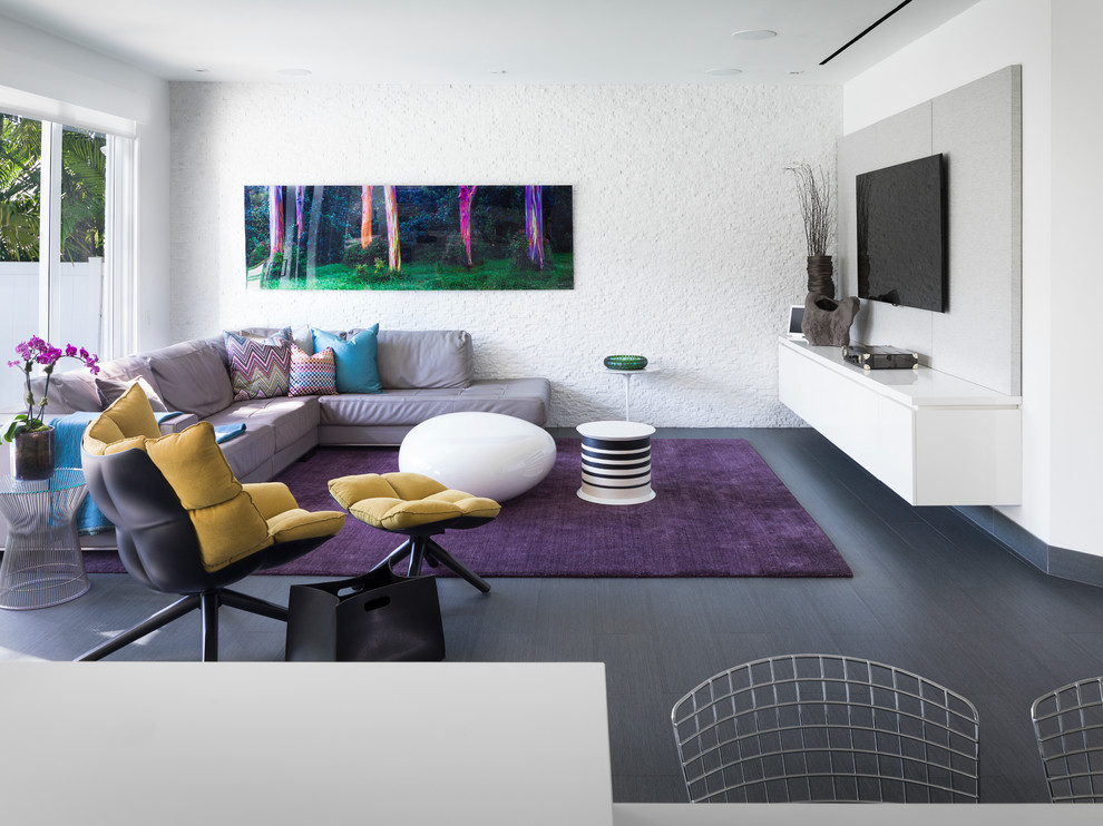 This is an example of a contemporary open concept family room in Miami with white walls, a wall-mounted tv, dark hardwood floors and grey floor.