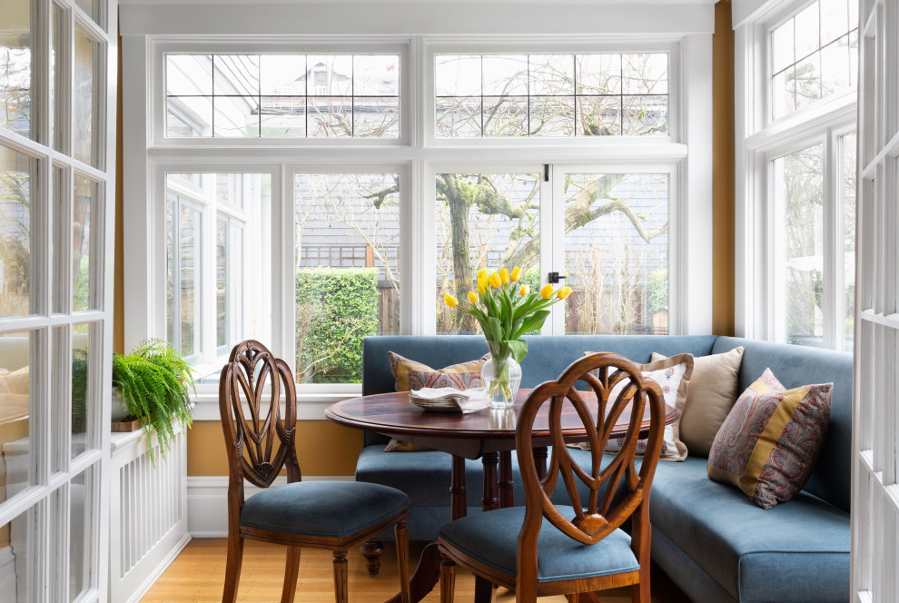 Design ideas for a small classic dining room in Seattle with banquette seating, yellow walls, light hardwood flooring, no fireplace and a tiled fireplace surround.