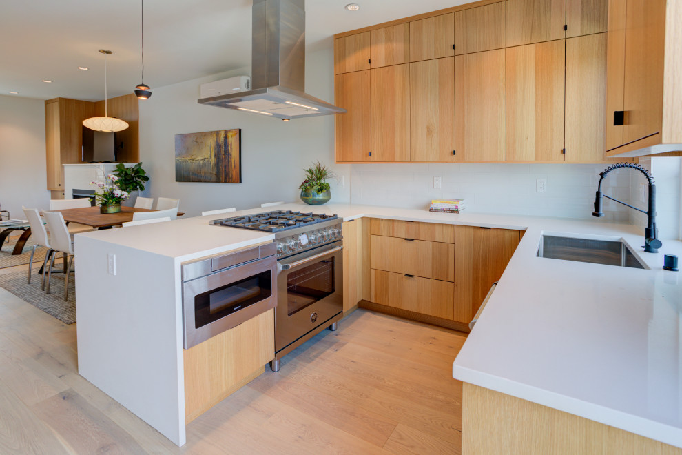 Design ideas for a mid-sized modern u-shaped eat-in kitchen in Seattle with an undermount sink, flat-panel cabinets, light wood cabinets, quartz benchtops, white splashback, porcelain splashback, stainless steel appliances, light hardwood floors, no island and white benchtop.