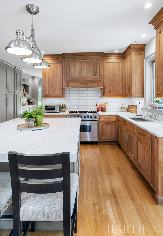 Mid-sized transitional l-shaped open plan kitchen in Philadelphia with an undermount sink, beaded inset cabinets, medium wood cabinets, quartz benchtops, white splashback, subway tile splashback, stainless steel appliances, light hardwood floors, with island, brown floor, white benchtop and vaulted.