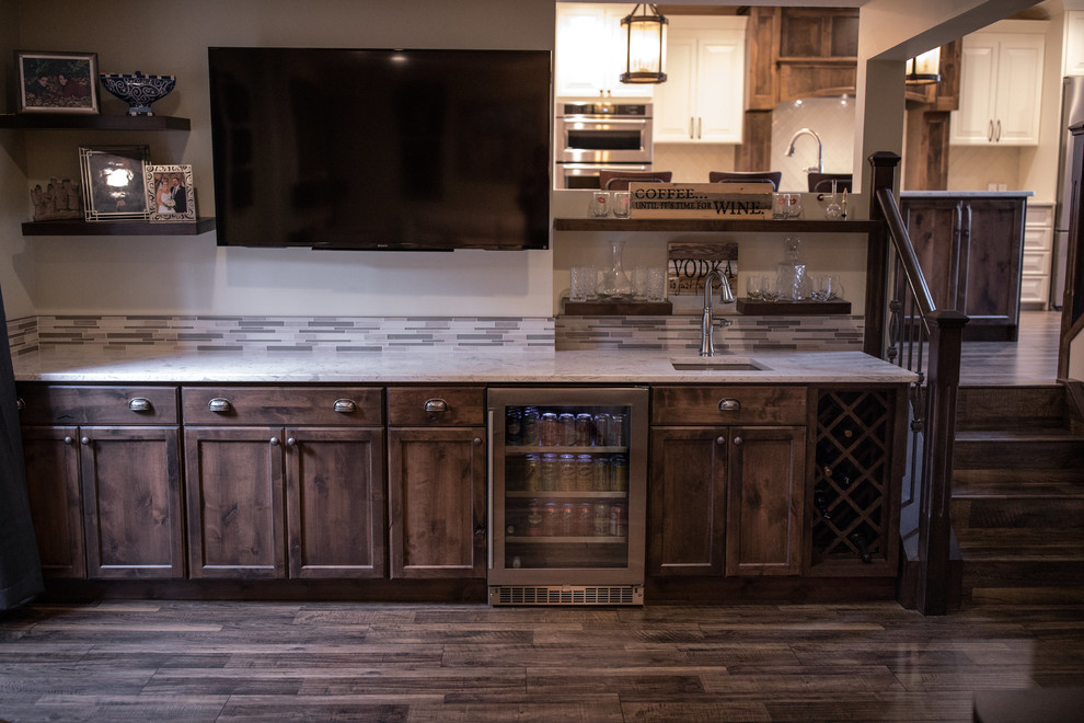 Inspiration for a large arts and crafts single-wall wet bar in Calgary with an undermount sink, shaker cabinets, dark wood cabinets, quartz benchtops, grey splashback, glass tile splashback, laminate floors and brown floor.