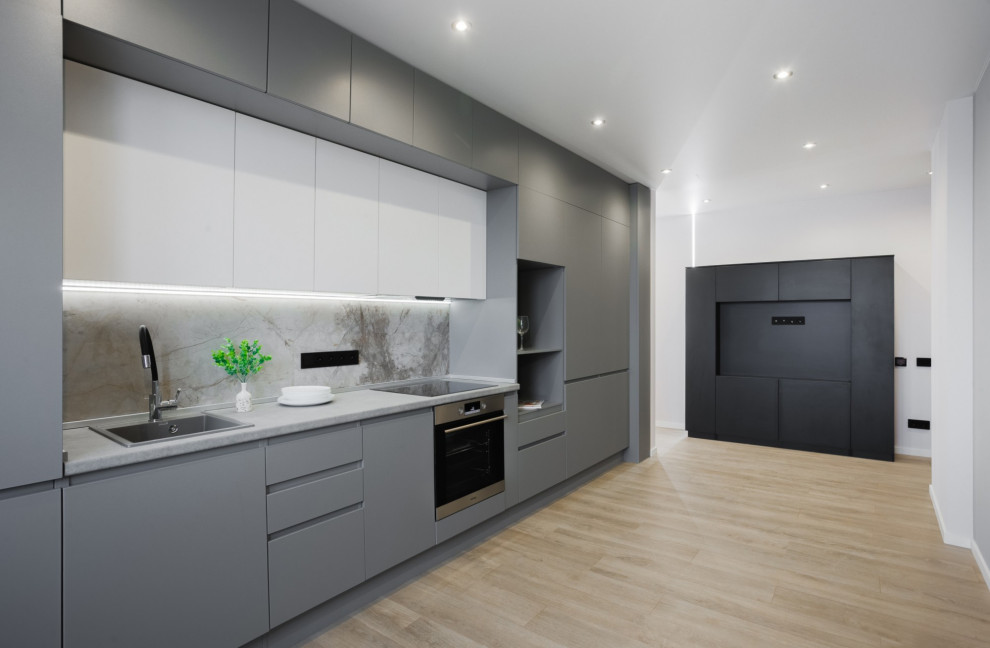 This is an example of a mid-sized contemporary single-wall open plan kitchen in Other with a drop-in sink, flat-panel cabinets, grey cabinets, grey splashback, stainless steel appliances, laminate floors, no island, beige floor and grey benchtop.