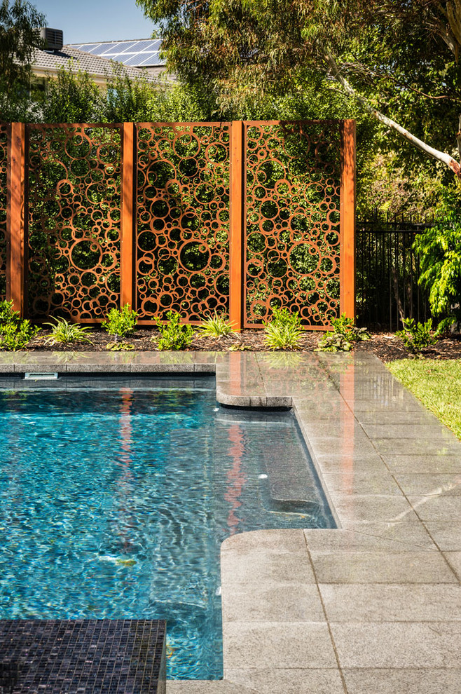 This is an example of a mid-sized contemporary backyard rectangular lap pool in Melbourne with a hot tub and natural stone pavers.
