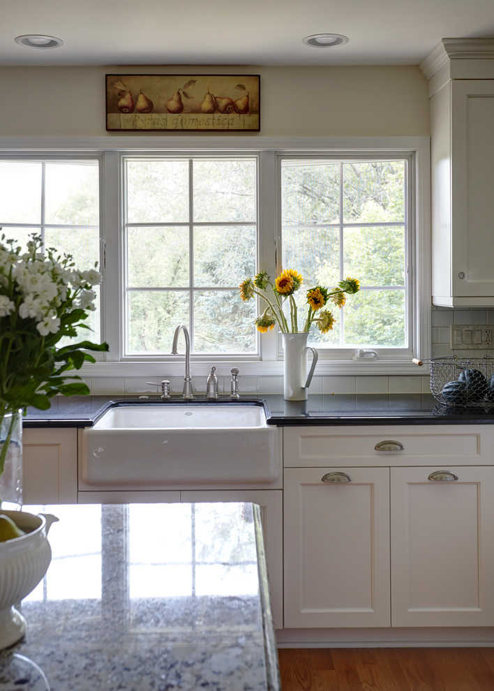 Inspiration for a large transitional l-shaped light wood floor enclosed kitchen remodel in Chicago with a farmhouse sink, white cabinets, granite countertops, white backsplash, stainless steel appliances, an island, shaker cabinets and subway tile backsplash