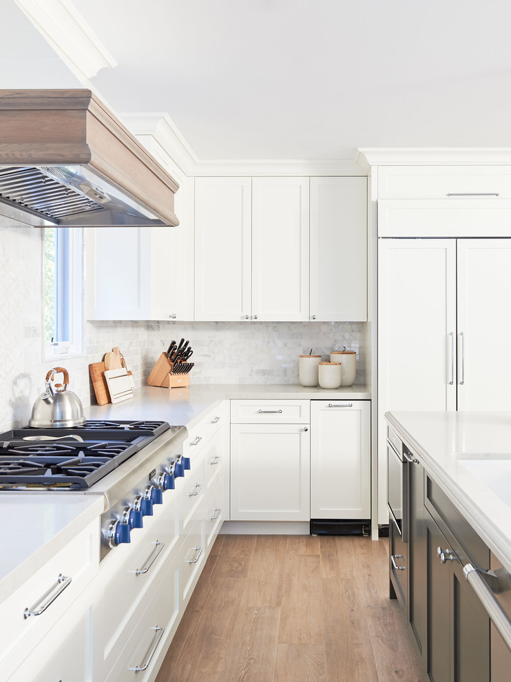 Large beach style u-shaped open plan kitchen in San Diego with a farmhouse sink, shaker cabinets, white cabinets, quartz benchtops, white splashback, marble splashback, panelled appliances, ceramic floors, multiple islands, brown floor and white benchtop.