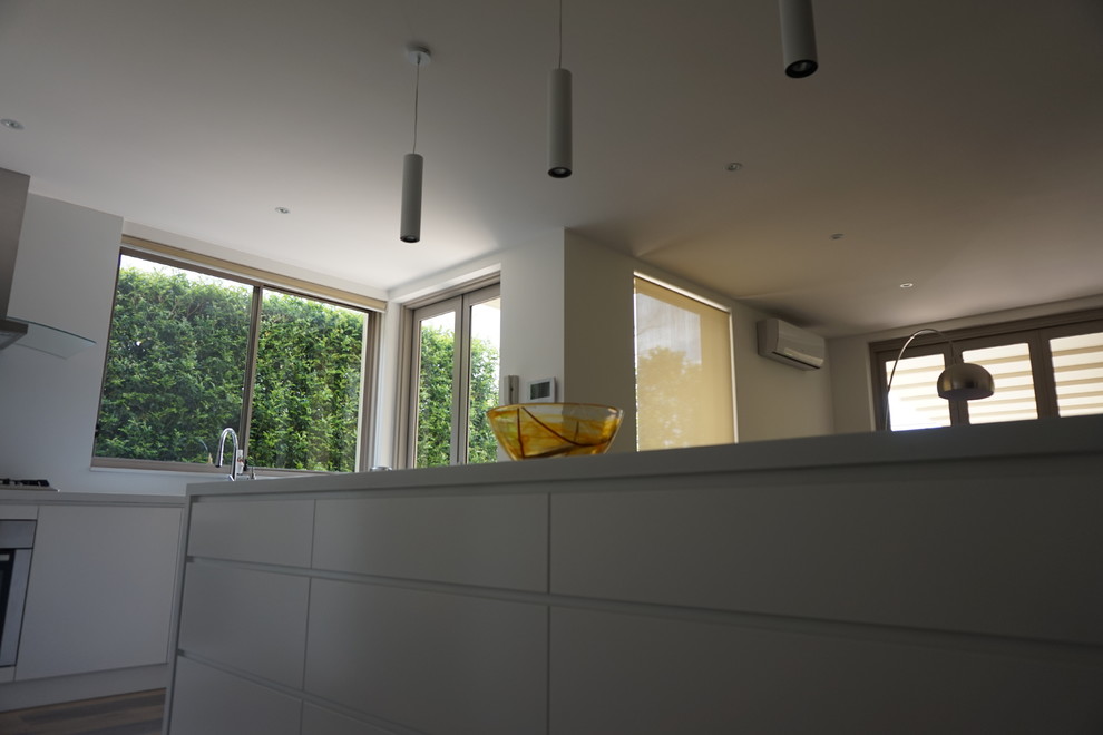 Design ideas for a mid-sized modern l-shaped eat-in kitchen in Sydney with an undermount sink, flat-panel cabinets, white cabinets, quartz benchtops, white splashback, stainless steel appliances, ceramic floors, with island and glass sheet splashback.