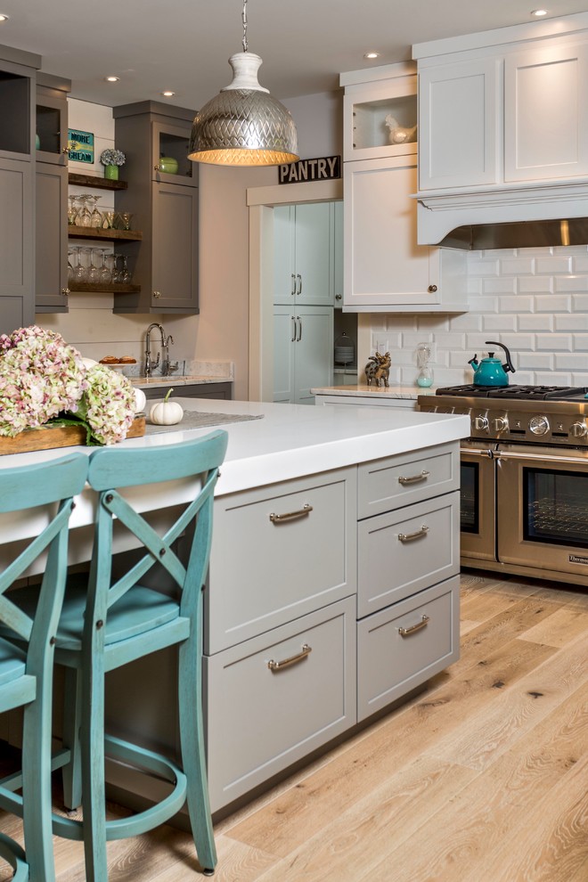 Large arts and crafts u-shaped open plan kitchen in Portland Maine with a farmhouse sink, recessed-panel cabinets, white cabinets, quartz benchtops, white splashback, subway tile splashback, stainless steel appliances, light hardwood floors and with island.