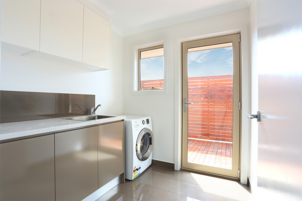 Photo of a mid-sized modern single-wall dedicated laundry room in Melbourne with a drop-in sink, flat-panel cabinets, brown cabinets, quartz benchtops, white walls, porcelain floors and a side-by-side washer and dryer.