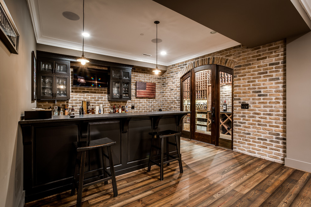 This is an example of a large arts and crafts galley wet bar in DC Metro with glass-front cabinets, dark wood cabinets, wood benchtops, red splashback, stone tile splashback and medium hardwood floors.