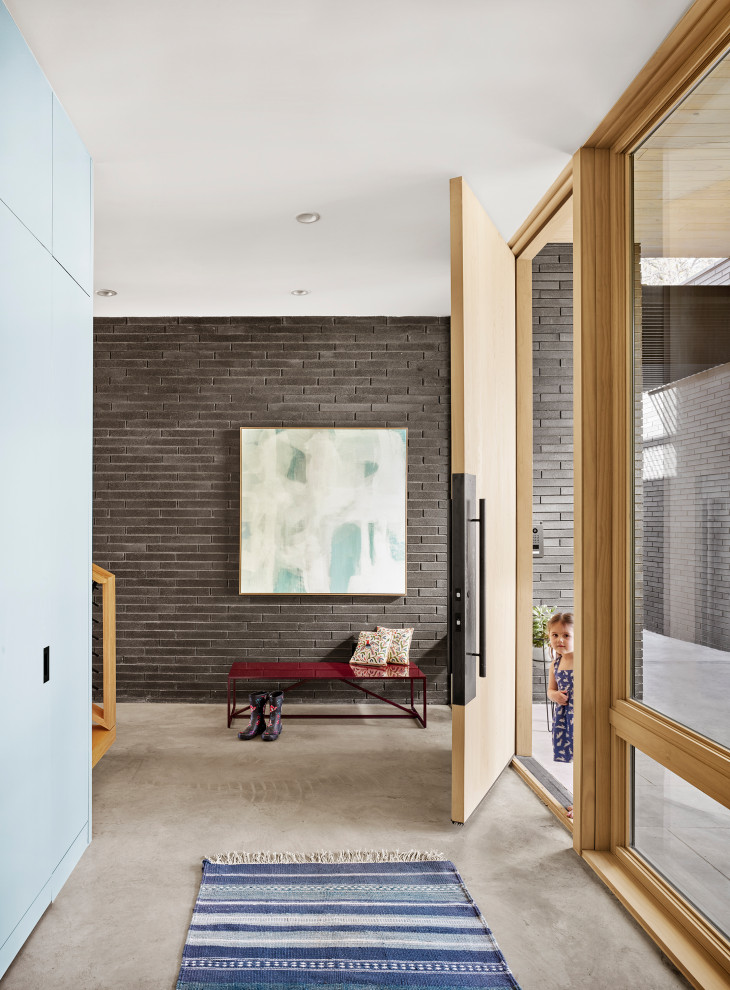 This is an example of a midcentury entryway in Austin with black walls, concrete floors, a single front door, a light wood front door, grey floor and brick walls.