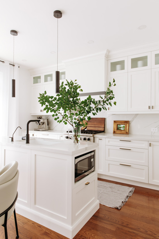 Eat-in kitchen - mid-sized transitional l-shaped dark wood floor and brown floor eat-in kitchen idea in Toronto with an undermount sink, shaker cabinets, white cabinets, quartz countertops, white backsplash, quartz backsplash, black appliances, an island and white countertops