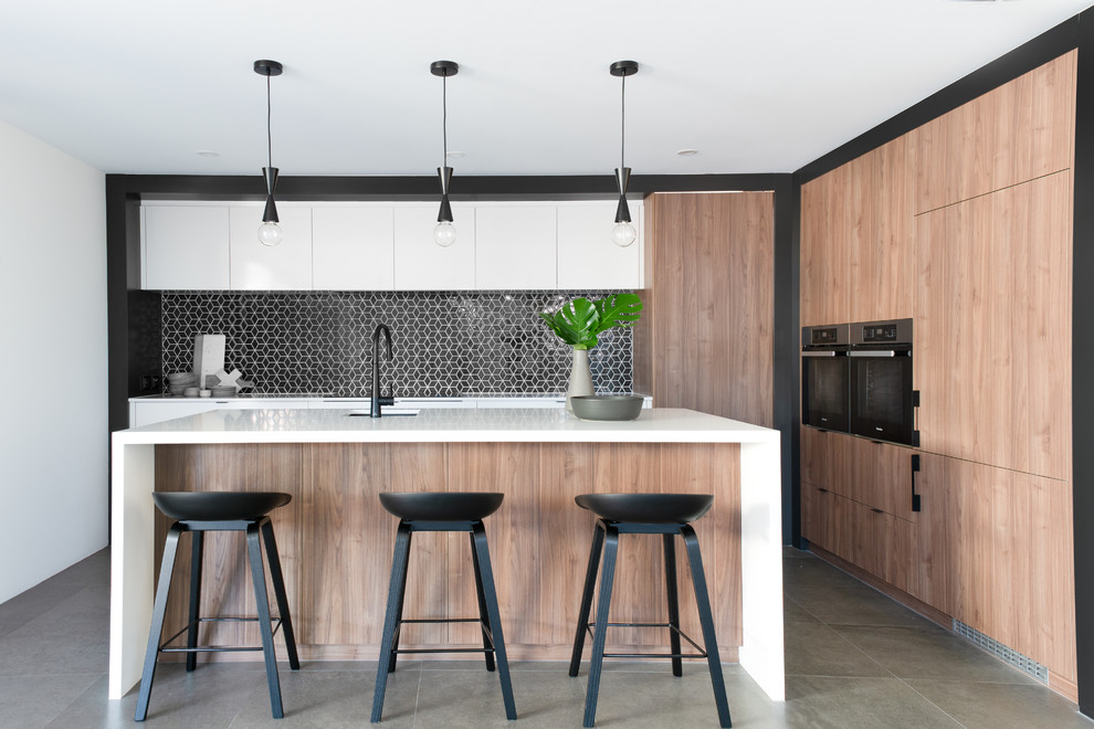 Design ideas for a contemporary l-shaped kitchen in Perth with an undermount sink, flat-panel cabinets, white cabinets, black splashback, black appliances, with island, grey floor and white benchtop.