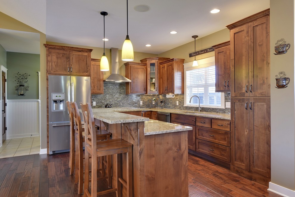 Photo of a large arts and crafts l-shaped open plan kitchen in Minneapolis with an undermount sink, recessed-panel cabinets, dark wood cabinets, granite benchtops, grey splashback, glass tile splashback, stainless steel appliances, medium hardwood floors and with island.