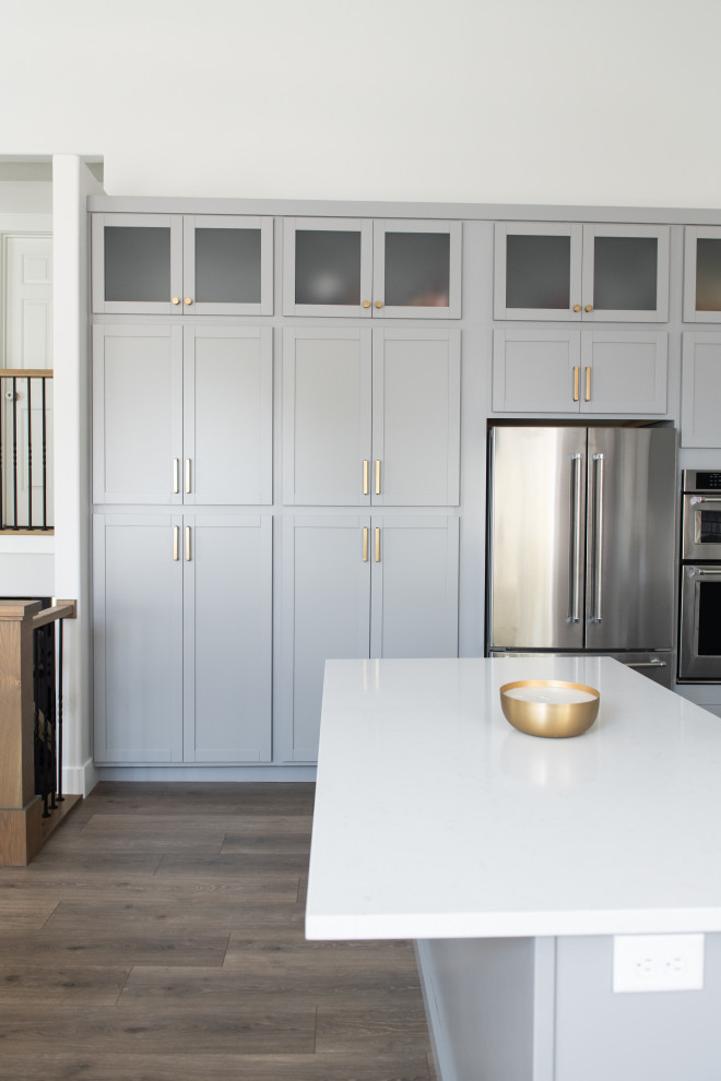 Inspiration for a mid-sized beach style l-shaped eat-in kitchen in Salt Lake City with shaker cabinets, quartz benchtops, with island, white benchtop, an undermount sink, blue cabinets, white splashback, ceramic splashback, stainless steel appliances, laminate floors and brown floor.