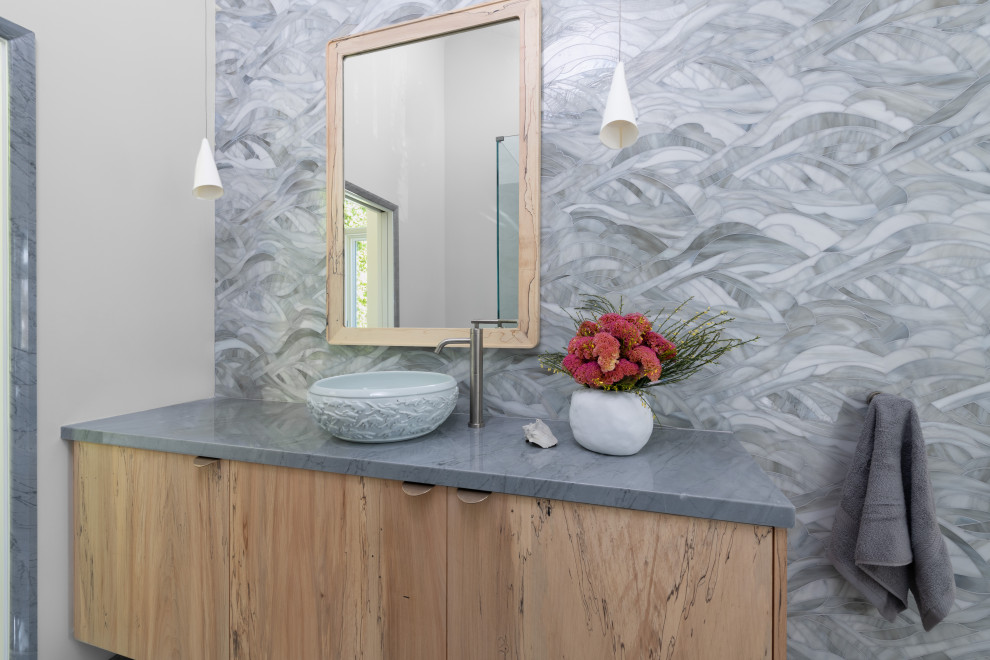 Large beach style bathroom in Los Angeles with flat-panel cabinets, light wood cabinets, a japanese tub, an alcove shower, a one-piece toilet, gray tile, glass tile, grey walls, marble floors, a vessel sink, marble benchtops, grey floor, grey benchtops, a shower seat, a single vanity and a floating vanity.