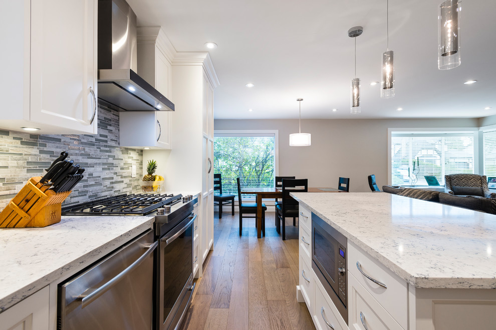 Open concept kitchen - mid-sized transitional l-shaped light wood floor and brown floor open concept kitchen idea in Vancouver with an undermount sink, shaker cabinets, white cabinets, quartz countertops, multicolored backsplash, mosaic tile backsplash, stainless steel appliances and an island