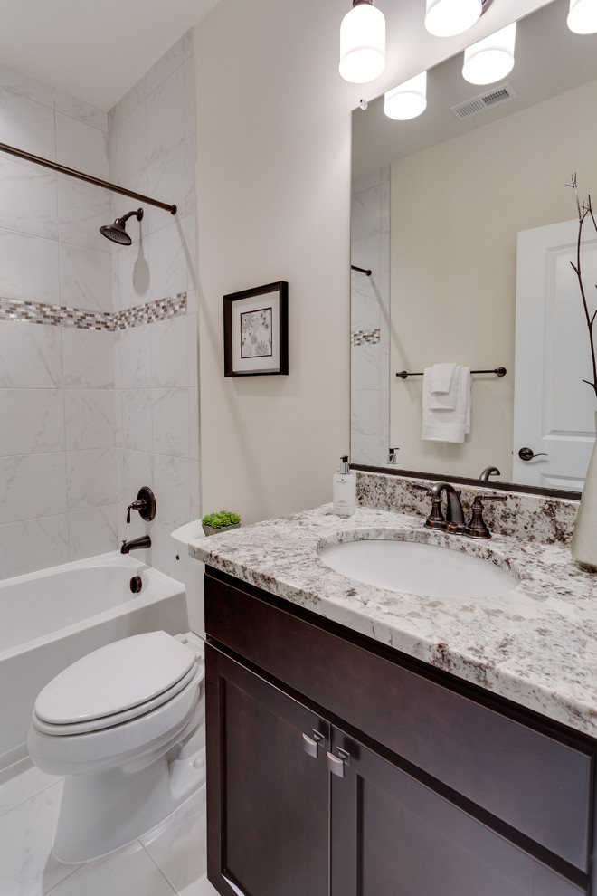 Photo of a mid-sized traditional bathroom in DC Metro with shaker cabinets, dark wood cabinets, a shower/bathtub combo, a two-piece toilet, black and white tile, gray tile, marble, marble floors, an undermount sink, granite benchtops, grey floor and brown walls.