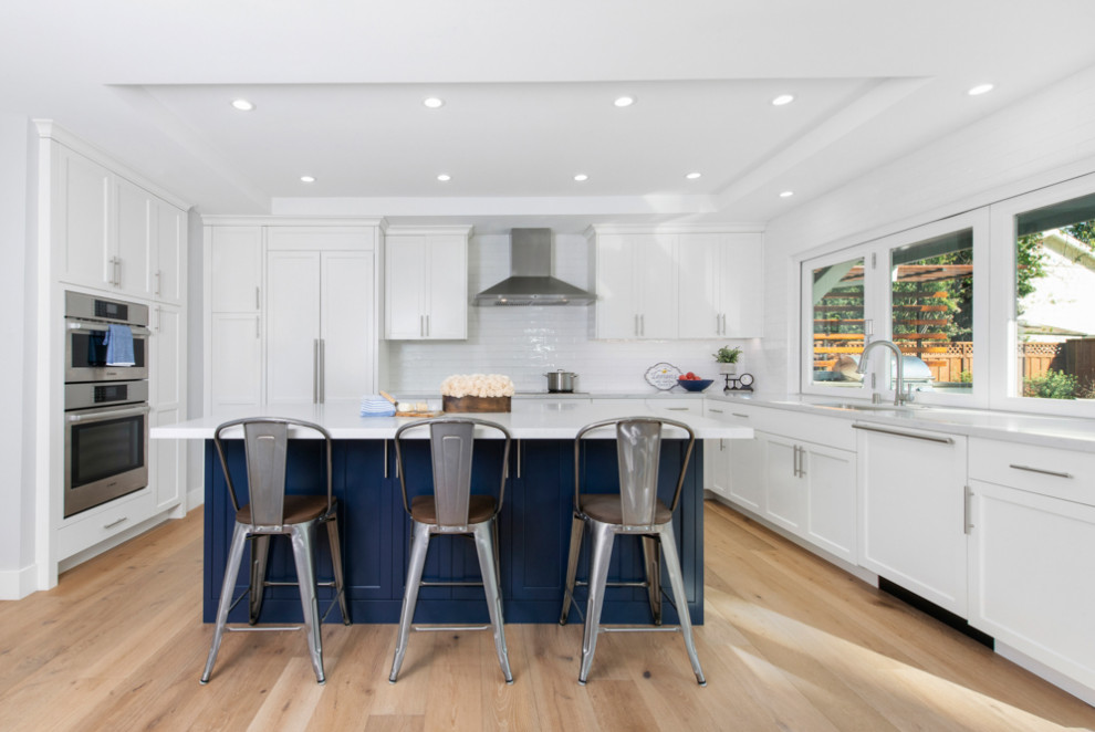This is an example of a mid-sized transitional u-shaped open plan kitchen in San Francisco with an undermount sink, shaker cabinets, white cabinets, quartz benchtops, white splashback, ceramic splashback, stainless steel appliances, light hardwood floors, with island, brown floor, white benchtop and coffered.