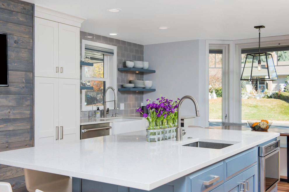 Example of a large transitional u-shaped light wood floor enclosed kitchen design in Denver with a farmhouse sink, shaker cabinets, white cabinets, quartz countertops, gray backsplash, ceramic backsplash, stainless steel appliances and an island