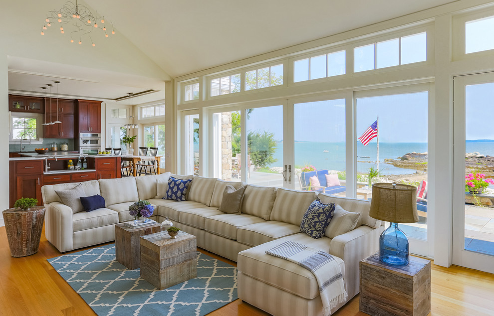 Inspiration for a large beach style open concept living room in Boston with white walls, light hardwood floors, a standard fireplace, a stone fireplace surround, a wall-mounted tv and brown floor.