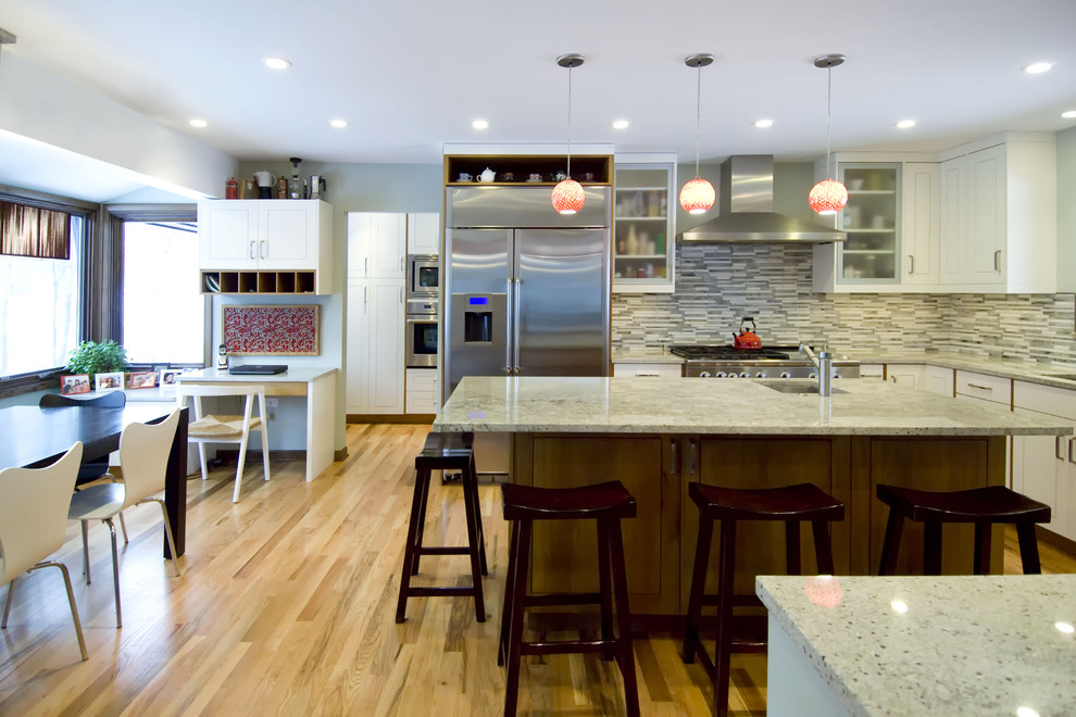 This is an example of a contemporary l-shaped eat-in kitchen in Chicago with stainless steel appliances, granite benchtops, glass-front cabinets, white cabinets, grey splashback and matchstick tile splashback.