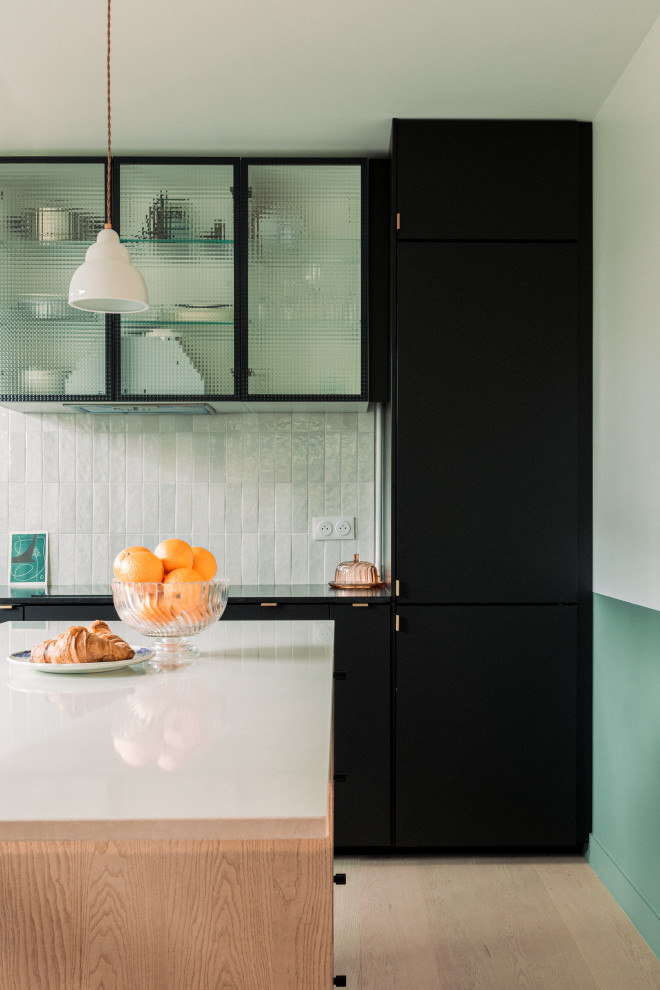 Foto på ett stort funkis svart kök, med en undermonterad diskho, luckor med glaspanel, svarta skåp, bänkskiva i kvartsit, vitt stänkskydd, stänkskydd i keramik, integrerade vitvaror, ljust trägolv, en köksö och brunt golv