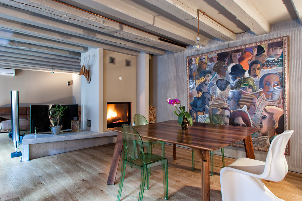 Inspiration for a mid-sized industrial open plan dining in Other with a two-sided fireplace, a plaster fireplace surround and light hardwood floors.