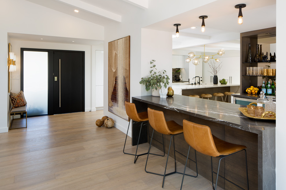 Photo of a midcentury galley seated home bar in San Diego with flat-panel cabinets, black cabinets, marble benchtops, mirror splashback, light hardwood floors, beige floor and black benchtop.