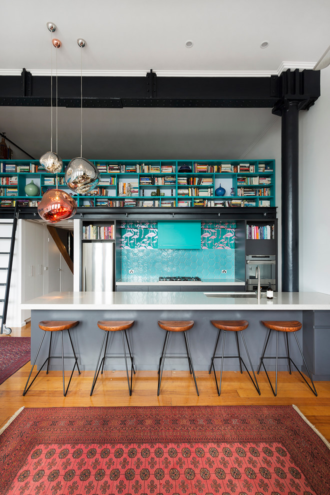 This is an example of a mid-sized industrial galley eat-in kitchen in Melbourne with an undermount sink, flat-panel cabinets, grey cabinets, quartz benchtops, blue splashback, ceramic splashback, stainless steel appliances and medium hardwood floors.
