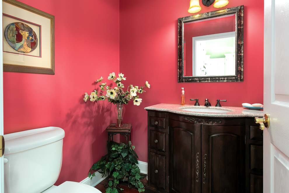 This is an example of a small traditional powder room in Philadelphia with raised-panel cabinets, dark wood cabinets, red walls, dark hardwood floors, an undermount sink, granite benchtops and brown floor.