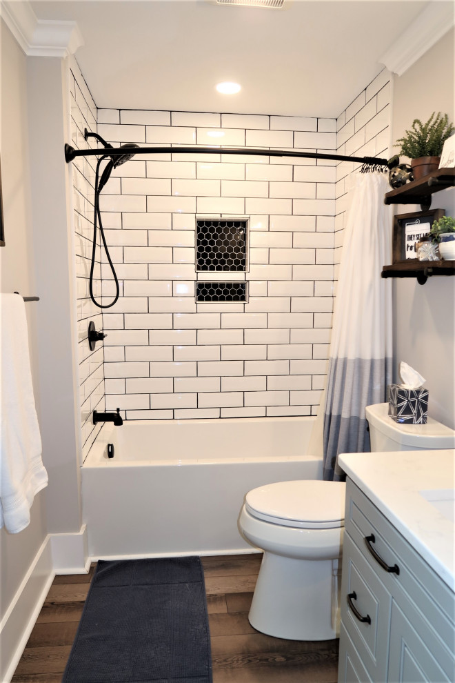 Inredning av ett modernt stort vit vitt badrum för barn, med luckor med upphöjd panel, grå skåp, ett badkar i en alkov, en dusch/badkar-kombination, en toalettstol med separat cisternkåpa, vit kakel, keramikplattor, grå väggar, mörkt trägolv, bänkskiva i kvarts, brunt golv och dusch med duschdraperi