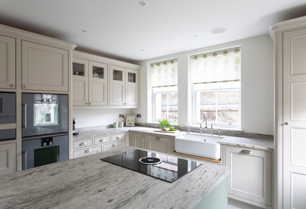 Inspiration for a mid-sized transitional l-shaped kitchen in Edinburgh with a farmhouse sink, recessed-panel cabinets, beige cabinets, beige splashback, black appliances, with island and beige benchtop.