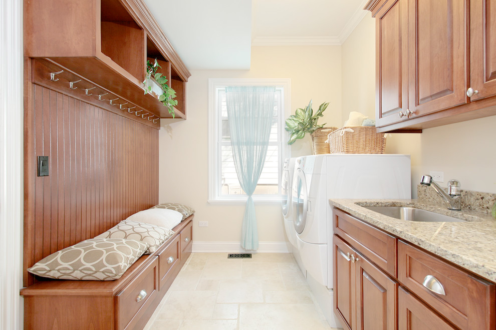 This is an example of a traditional laundry room in Chicago with raised-panel cabinets, medium wood cabinets, a side-by-side washer and dryer, an undermount sink, beige floor and beige walls.