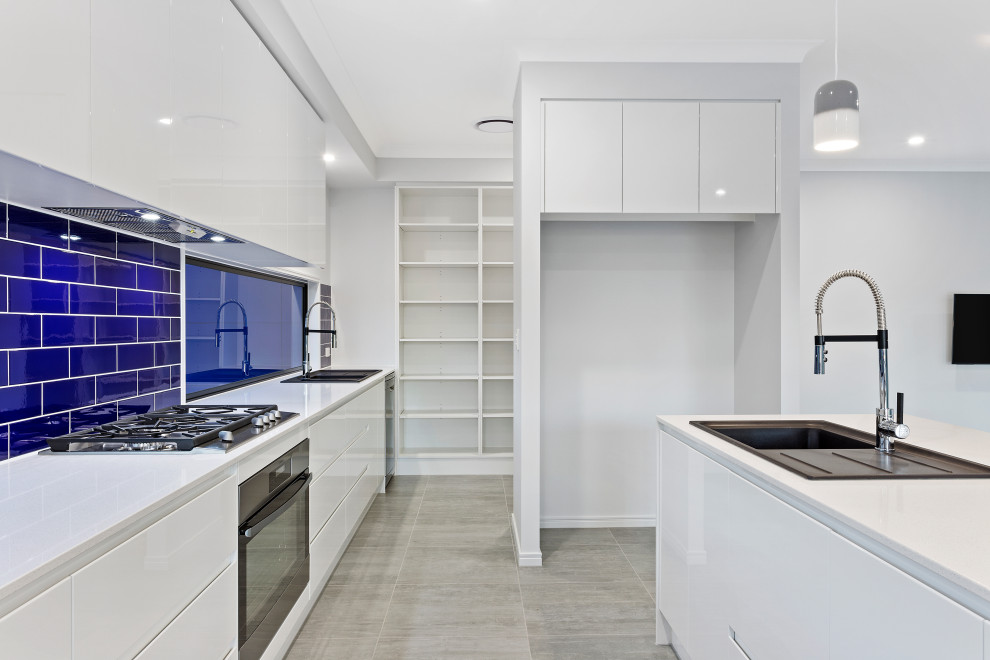 Inspiration for a mid-sized galley open plan kitchen in Brisbane with a drop-in sink, shaker cabinets, white cabinets, quartz benchtops, blue splashback, subway tile splashback, black appliances, porcelain floors, with island, grey floor and white benchtop.