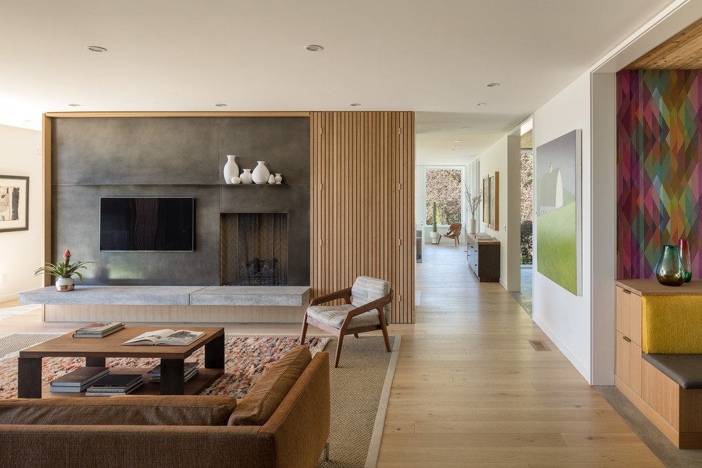 Photo of a midcentury open concept living room in Portland with white walls, medium hardwood floors, a standard fireplace, a wall-mounted tv and brown floor.