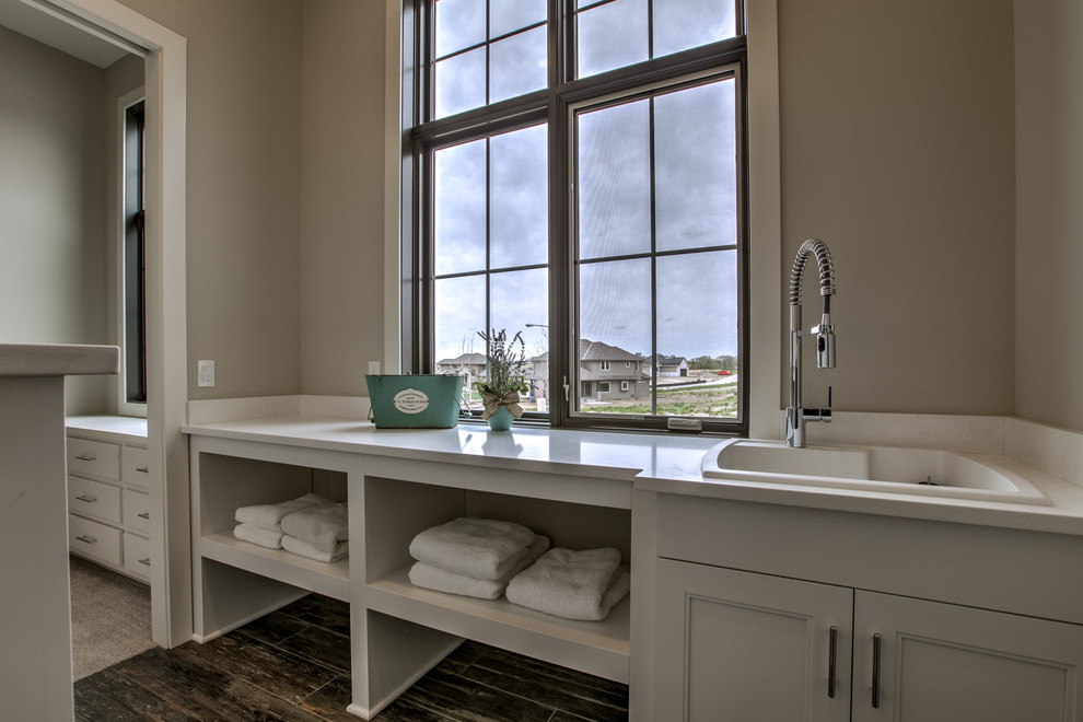 Design ideas for a large country single-wall dedicated laundry room in Omaha with a drop-in sink, quartzite benchtops, porcelain floors, a side-by-side washer and dryer, white cabinets, recessed-panel cabinets, grey walls and grey floor.
