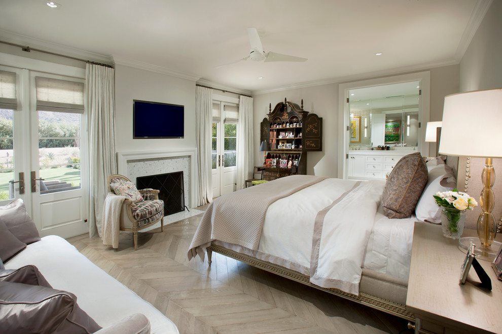 This is an example of a master bedroom in Los Angeles with beige walls, light hardwood floors and a standard fireplace.