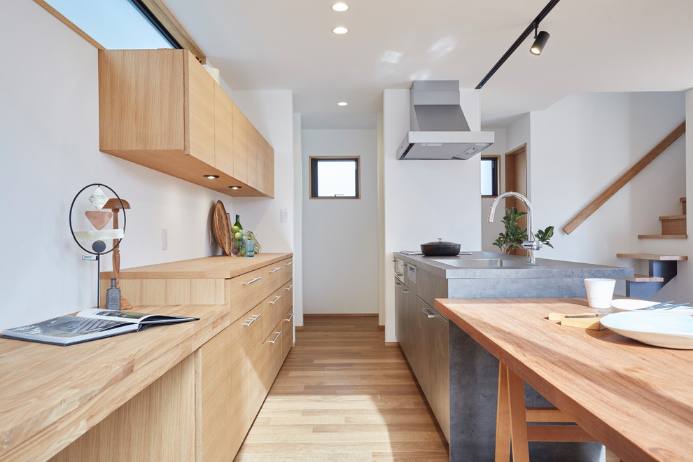 Contemporary galley open plan kitchen in Tokyo with white splashback, brown floor, flat-panel cabinets, light wood cabinets, wood benchtops, panelled appliances, light hardwood floors and brown benchtop.