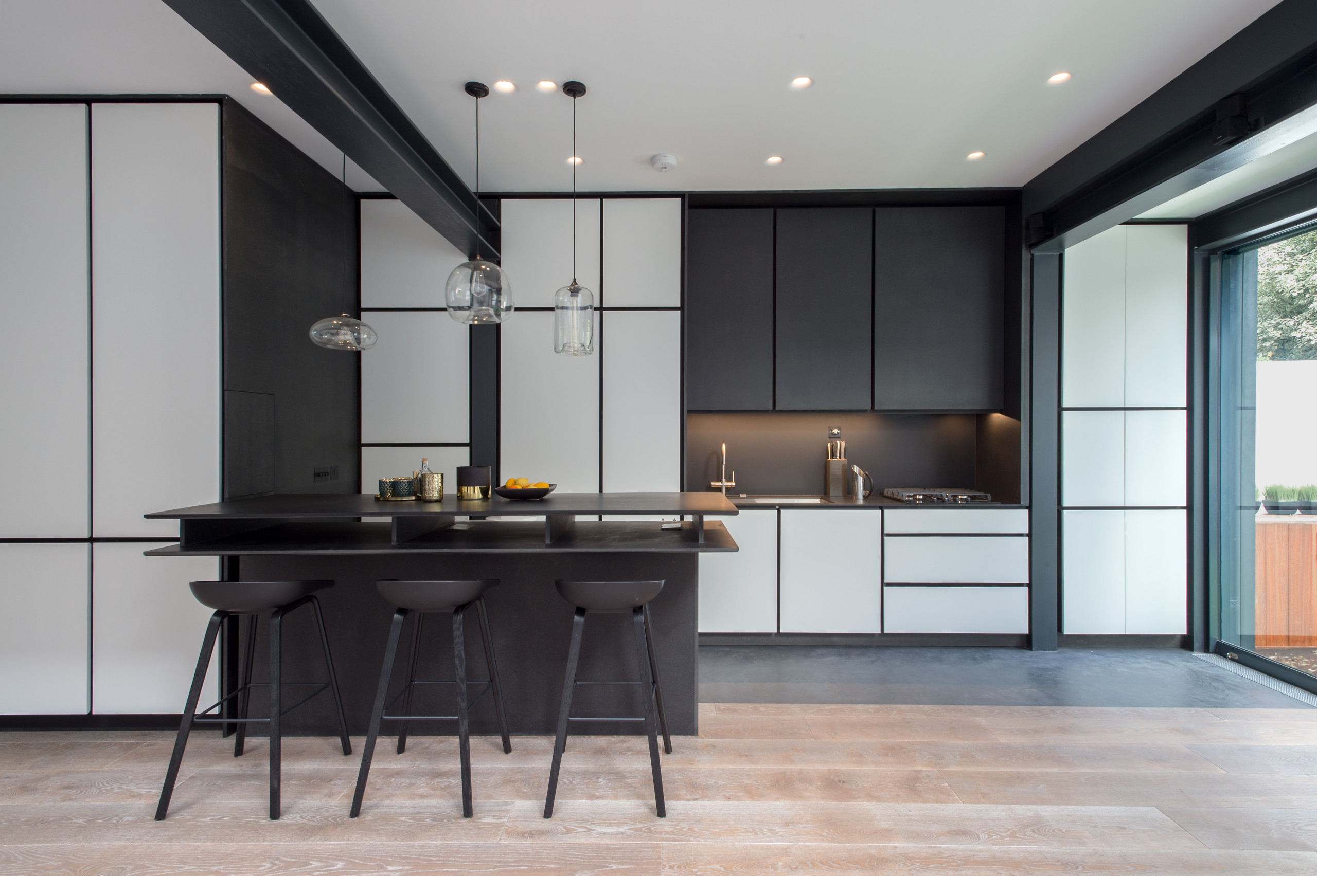 Minimalist modern black & white kitchen with black recess handles for edginess and sharp look. We've capitalised on black architectural steel beams to maximise height and glass/sun. the chosen monochr