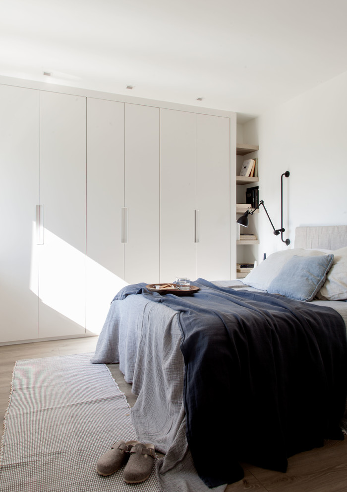 This is an example of a contemporary bedroom in Bilbao with white walls, medium hardwood floors and brown floor.